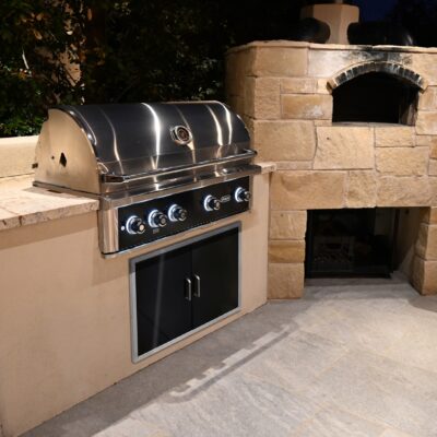 Wildfire Outdoor Living 42" Ranch Pro Luxury Gas Grill Closed, Island Angle, Built-In with Black Stainless Steel Double Door in Phoenix Patio with Pizza Oven At Night.
